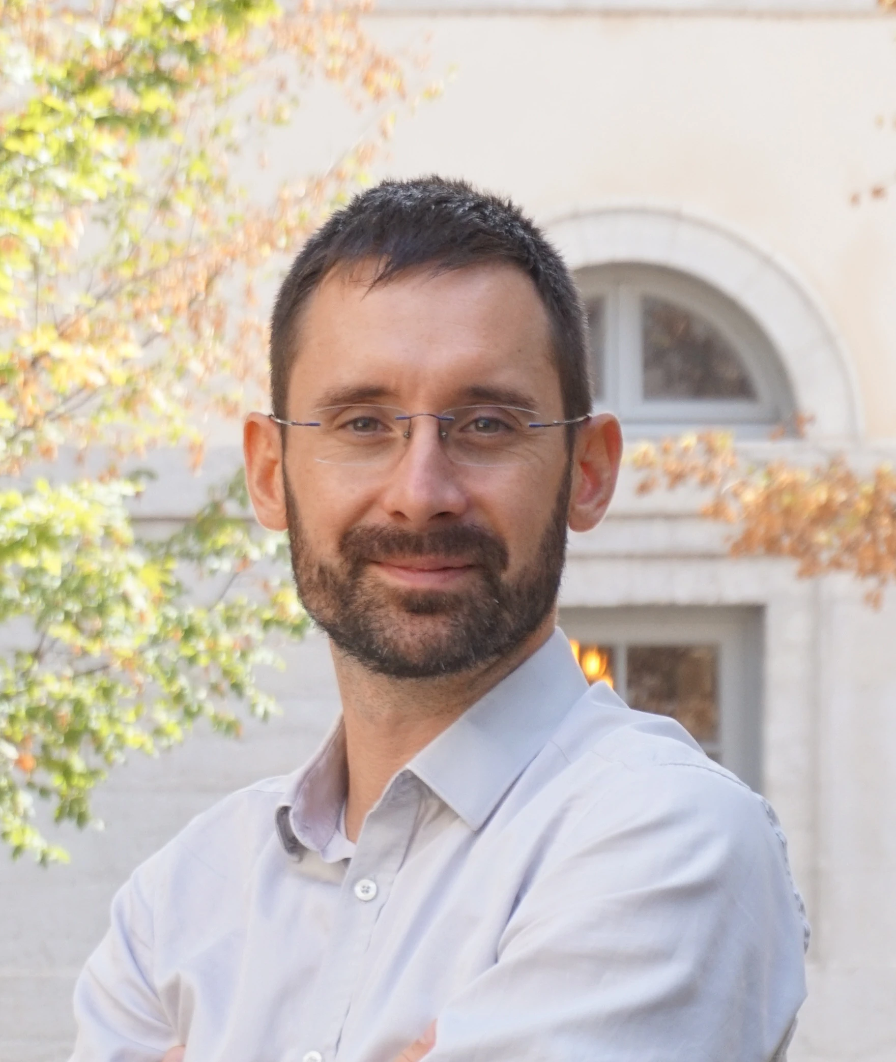 Thomas Lunardo souriant dans une chemise blanche avec un mur et un arbre en arrière-plan